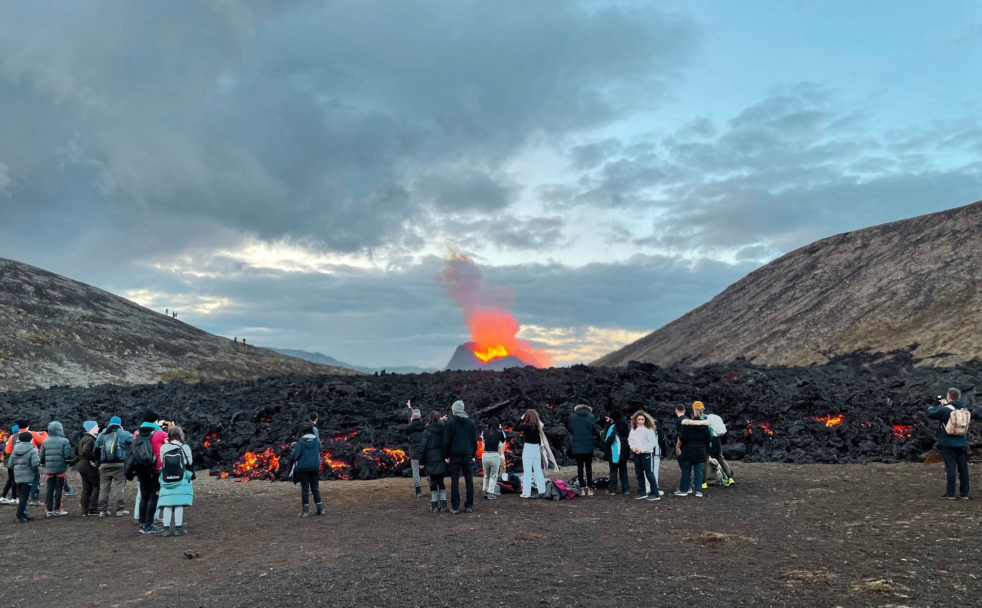 Við eldgos, ferðamenn standa við hraunjaðarinn og taka myndir