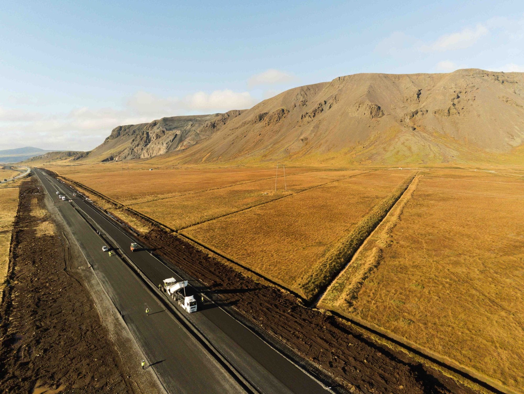 View of construction on the road next to a grassy area with ditches and mountains