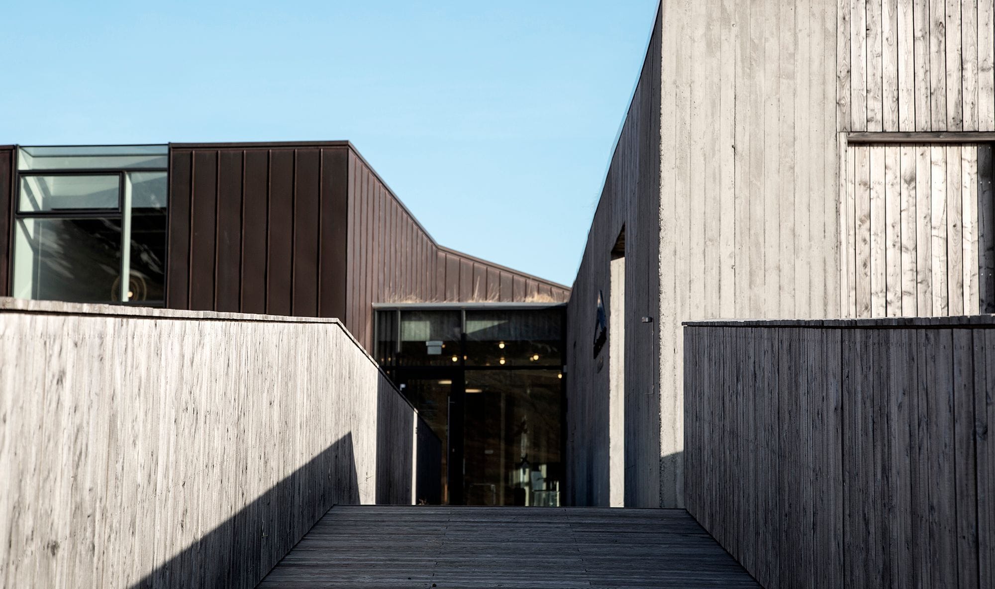 Entrance to a modern wooden building, stairs leading up to the main entrance, blue sky in the background